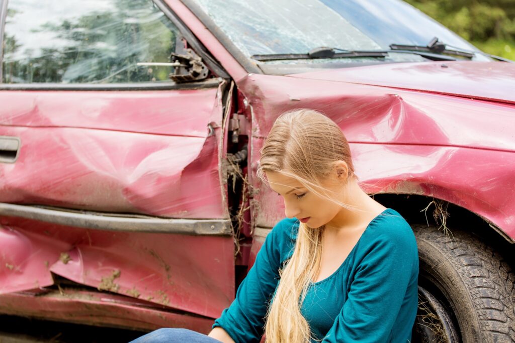 teenager sitting next to a car after being in an accident