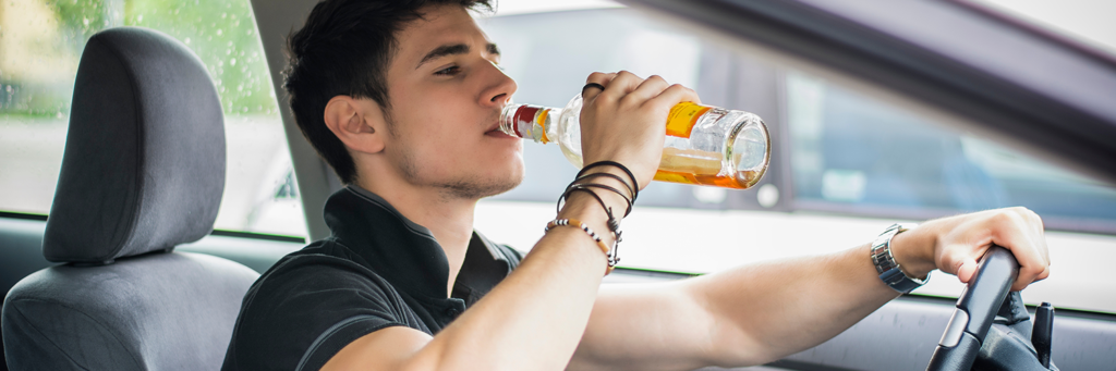 Young man driving his car while drinking alcohol.