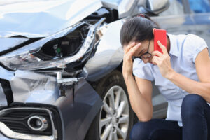 A woman sitting next to her car as she calls her car accident attorney on the phone after experiencing a hit-and-run in El Paso.