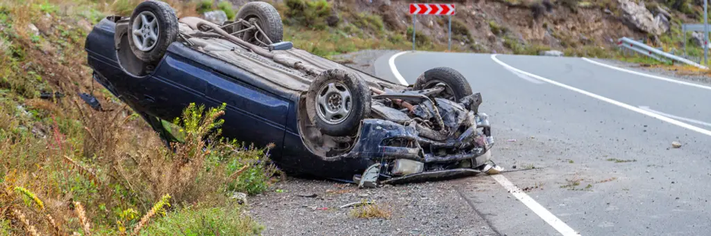 Car accident place on a bend, overturned car lies on the roof.